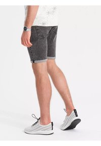 Shorts en jean gris avec ourlets retroussés, poches avant et arrière. Portés avec des baskets blanches perforées et une chemise à motifs légers.