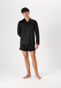 Svart satin skjorta med långa ärmar, framficka och matchande svarta shorts, med en avslappnad passform och slät textur.