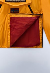 Yellow jacket featuring a mesh red inner pocket and a small patch with a flag design. Zipper and fabric texture are visible.