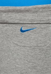 Tessuto in misto cotone grigio con una texture liscia, caratterizzato da un piccolo logo Nike swoosh blu e un sottile dettaglio della tasca.