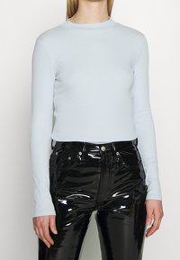 Ljusblå långärmad topp i ribbat material med rund halsringning. Tillsammans med högglansiga svarta vinylbyxor med synliga sömmar och fickor.