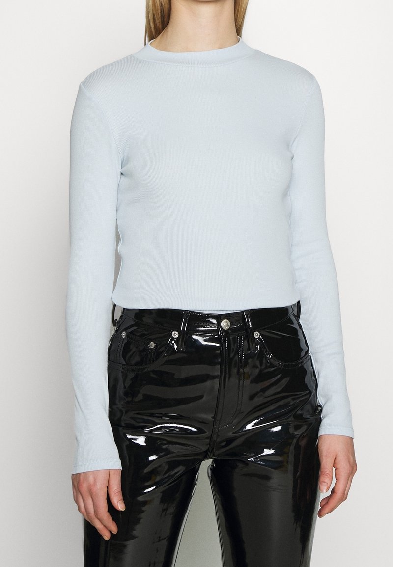 Ljusblå långärmad topp i ribbat material med rund halsringning. Tillsammans med högglansiga svarta vinylbyxor med synliga sömmar och fickor.