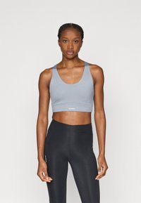 Ανοιχτό μπλε αθλητικό σουτιέν με στρογγυλή λαιμόκοψη και φαρδιές τιράντες, συνδυασμένο με μαύρο κολάν ψηλόμεσο με ματ τελείωμα.