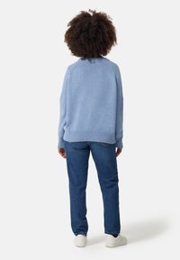 Hellblaues, übergroßes Sweatshirt mit geripptem Saum und Bündchen, kombiniert mit dunkelblauen Jeans und weißen Schuhen. Sicht von hinten.