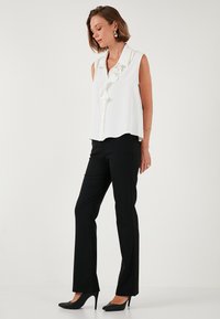 White sleeveless blouse with ruffled front, paired with black slim-fit trousers and black heels, showcasing a clean and sleek design.