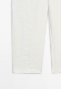 Närbild av vita byxor med raka ben och texturerat tygmaterial.