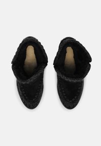 Botas de tobillo de ante negro con un interior suave y texturizado, que presentan un ribete trenzado a lo largo de la abertura y un diseño de punta redondeada.