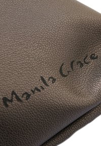 Materiale in finta pelle marrone con texture, caratterizzato dal nome del marchio "Manila Grace" in rilievo scritto in un carattere moderno sulla superficie.