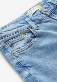 Ljusblå bootcut-jeans i denim med en texturerad yta. Har en liten ficka, kopparnitar och en orange etikett i midjan.
