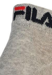 Szürke pamut zokni textúrált felülettel, amelyen egy sötétkék "FILA" logó található, a logó felett pedig piros díszítés a szegélyen.
