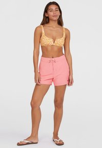 Gul mönstrad bikinitopp med breda axelband och djup urringning, i kombination med ljusrosa shorts med dragsko i midjan och logodetalj.