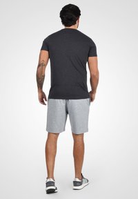 T-shirt gris charbon pour homme à manches courtes, associé à un short gris clair. La tenue est complétée par des baskets grises et noires.