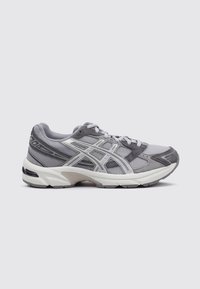 Baskets de sport grises avec une tige en mesh, des accents en suede et une semelle blanche. Elles disposent de lacets et d'un logo distinctif sur le côté.