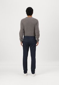 Grauer Strickpullover mit strukturiertem Stoff und Raglanärmeln, kombiniert mit blauen Hosen und weißen Sneakers, von hinten betrachtet.