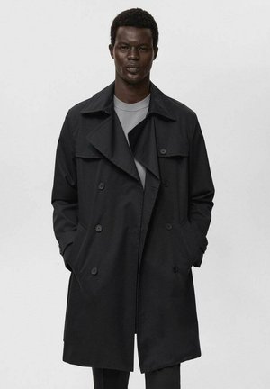 Abrigo negro de trench con un diseño de doble botonadura, amplias solapas y bolsillos laterales. Confeccionado en tela suave, presenta un estilo limpio y minimalista.