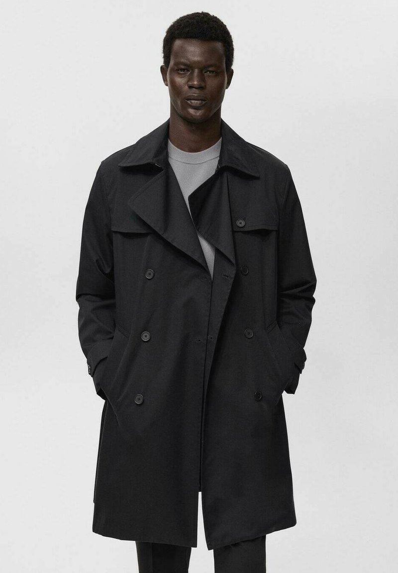 Abrigo negro de trench con un diseño de doble botonadura, amplias solapas y bolsillos laterales. Confeccionado en tela suave, presenta un estilo limpio y minimalista.