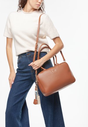 Bolso de mano de cuero marrón con textura suave y logotipo dorado. Cuenta con asas cortas y una correa de hombro desmontable. Acentuado con un llavero.