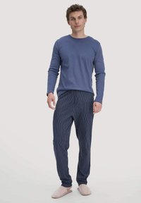 Navy- und weiß gestreifte Schlafanzughosen mit elastischem Bund, kombiniert mit einem einfarbigen blauen Langarmshirt und grauen Hausschuhen.
