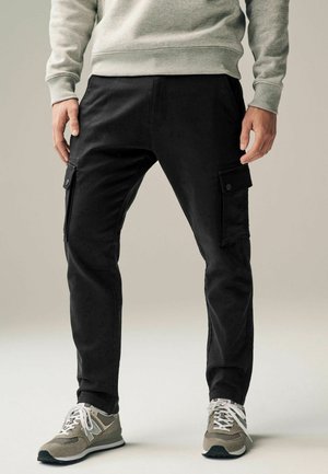 Svarta cargo-byxor med sidofickor, slim-fit design, blandning av bomullsmaterial och en jämn textur. Bärs med grå sneakers och en ljusgrå sweatshirt.