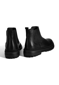 Bottines en cuir noir avec des panneaux latéraux élastiques, surface texturée, semelle en caoutchouc robuste et couture contrastante le long du bord de la semelle.