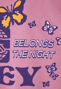 Růžové bavlněné tričko s motivem fialových a žlutých motýlů a nápisem „BELONGS THE NIGHT“ tučným stylizovaným písmem.