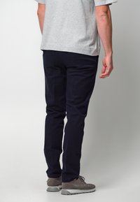 Marineblaue Hosen aus Baumwollmischgewebe, mit Slim-Fit-Schnitt und glatter Textur. Kombiniert mit grauen Schuhen und einem grauen T-Shirt.