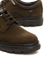 Chaussures en cuir marron avec une texture lisse, design à lacets, semelle en caoutchouc robuste et un subtil détail de couture. Présente une petite étiquette de logo.