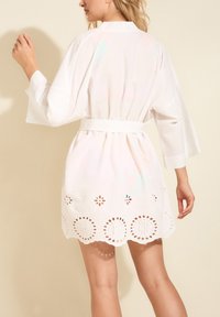 Biały bawełniany kimono z rękawami o długości trzech czwarte, z paskiem w talii i falbaniastym dołem, zdobiony haftem kółkowym i wycięciami w kwiaty.