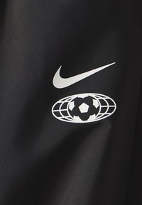 Svart tyg med en vit Nike-logotyp och en vit grafik av en fotboll inom en globdesign. Slät textur, minimalistisk design.