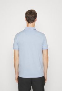 Světle modrá polokošile s krátkým rukávem, žebrovaným límcem a kontrastním lemováním na límci. Vyrobena z hladkého, prodyšného materiálu.