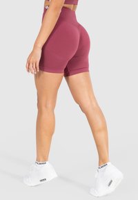 Shorts bordeaux a vita alta realizzati in tessuto elasticizzato, caratterizzati da una vestibilità aderente e orli rifiniti, abbinati a scarpe da ginnastica bianche.