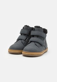 Bottes chevilles en cuir gris avec deux sangles Velcro ajustables, doublure en fourrure noire douce et semelles en caoutchouc avec un accent beige.