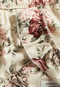 Bloemmotief stof met roze en kastanjebruine rozen op een crème achtergrond. Bevat gerimpelde randen en een label met de tekst "newbie".