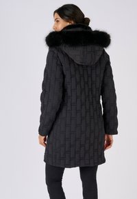 Zwarte donzen jas met een gestructureerd geweven patroon, met bont gevoerde capuchon en lange mouwen, voorzien van een knielange snit en een ontspannen pasvorm.