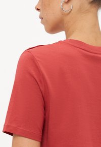 Rode katoenen t-shirt met korte mouwen, een ronde hals en decoratieve schouderknopen. Gladde textuur met een ontspannen pasvorm.