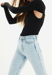 Bodysuit negro de manga larga con canalé y hombros descubiertos, combinado con pantalones vaqueros de cintura alta en denim azul claro. Presenta un diseño ajustado y cierre de botones.