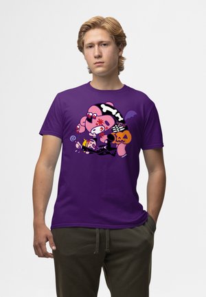 Jonge man met licht haar die een paars T-shirt draagt met een Halloween-thema cartoonvarken dat een pompoen en een lolly vasthoudt.