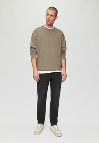 Grijze crewneck sweatshirt over een wit shirt, zwarte slim-fit jeans en beige sneakers. De sweatshirt heeft een geborduurd logo op de borst.