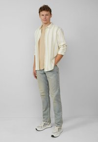 Jasnożółta, w paski, koszula na guziki noszona na beżowej koszulce, połączona z wyblakłymi niebieskimi dżinsami i szarymi butami sportowymi z czarnymi akcentami.