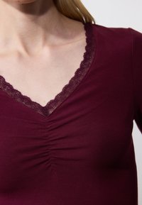 Mulberry v-neck top with lace trim and gathered detail at the bust, made from soft, stretchy fabric. Close-up of neckline and texture.