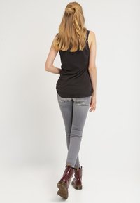 Top sin mangas negro, ajustado en la cintura, combinado con jeans skinny gris claro y botines burdeos con detalles texturizados.