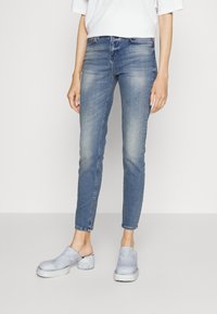 Vaqueros ajustados de un azul claro, hechos de denim, con un diseño desgastado, de cintura media y un estilo ligeramente cortado a la altura del tobillo. Combinados con zuecos ligeros en azul claro.