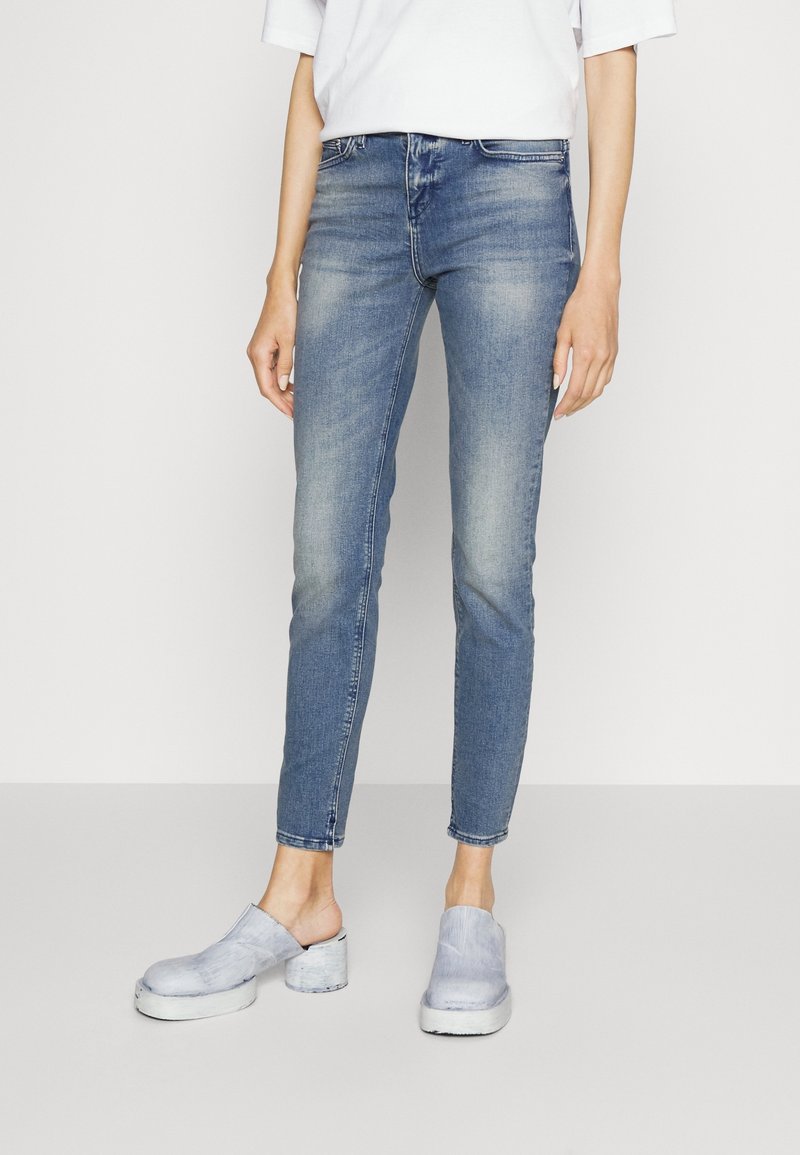 Vaqueros ajustados de un azul claro, hechos de denim, con un diseño desgastado, de cintura media y un estilo ligeramente cortado a la altura del tobillo. Combinados con zuecos ligeros en azul claro.
