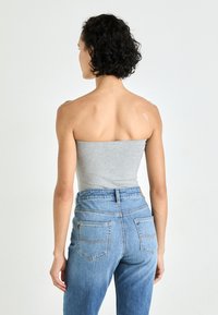 Grå off-shoulder topp med en tettsittende design, sammen med høyhøyde blå jeans med to baklommer og synlig søm.