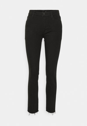 Mustat korkeavyötäröiset skinny-farkut, joissa nappi- ja vetoketjusuljin, viisi taskua ja rispaantuneet helmaukset yksivärisellä vaalealla taustalla.