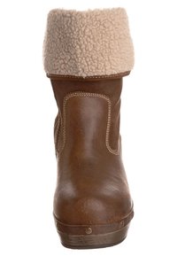 Ruskea nahkainen nilkkuri, jossa on beige tekoturkiskaulus, sileä pinta, pyöristetty kärki ja kontrastitikkaukset, metallikoristekivillä varustettu.