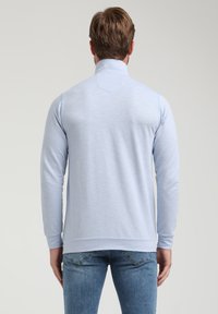 Pulóver de manga larga azul claro con cuello alto. Tejido texturizado y hombros sin costuras; diseño ajustado con puños y dobladillo de canalé.