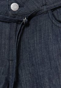 Jean en denim bleu foncé avec un bouton métallique étiqueté "PULL&BEAR" et une ceinture en tissu nouée passant à travers une double boucle métallique.