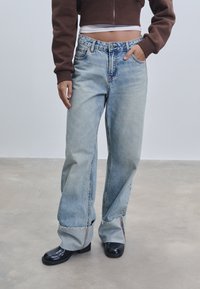 Svijetloplavi traperice širokog kroja s rastrganim rubom, visokim strukom i dva prednja džepa, u kombinaciji s crnim čizmama na petu i smešnim skraćenim puloverom.