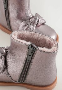 Metalliske lilla ankelstøvler med en sidezipper, blød pelsforing og en knude detaljer foran. Gummisål, glat tekstur.